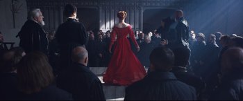 Movie still from “Mary Queen of Scots” (2018), directed by Josie Rourke – A woman in a red dress walking in front of a group of people; Wide shot, Over the shoulder angle