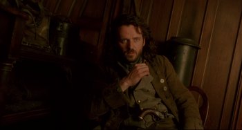 Movie still from “Frankenstein” (1994), directed by Kenneth Branagh – A man sitting in a chair wearing a jacket and hat; Medium shot, Low angle