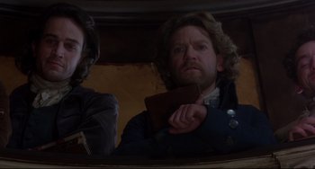 Movie still from “Frankenstein” (1994), directed by Kenneth Branagh – A man with a beard holding a book in front of another man with long hair; Medium shot, Low angle