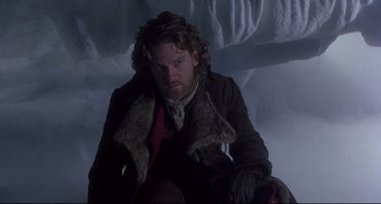 Movie still from “Frankenstein” (1994), directed by Kenneth Branagh – A man sitting on the ground wearing a coat and gloves; Medium shot, Low angle