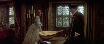 Movie still from “Mary, Queen of Scots” (1971), directed by Charles Jarrott – A man and a woman standing in front of a wooden bowl; Wide shot, High angle