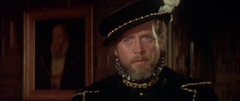 Movie still from “Mary, Queen of Scots” (1971), directed by Charles Jarrott – An older man wearing a black hat and a black coat; Close Up shot, Over the shoulder angle