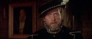 Movie still from “Mary, Queen of Scots” (1971), directed by Charles Jarrott – An older man with a beard wearing a hat; Close Up shot, Over the shoulder angle