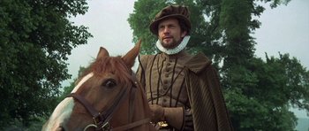 Movie still from “Mary, Queen of Scots” (1971), directed by Charles Jarrott – A man wearing a hat and a cape on top of a horse; Medium shot, Low angle