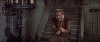 Movie still from “Mary, Queen of Scots” (1971), directed by Charles Jarrott – A man sitting on top of a wooden box; Medium shot, High angle