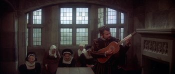 Movie still from “Mary, Queen of Scots” (1971), directed by Charles Jarrott – A man playing a guitar in front of a group of people; Wide shot, High angle