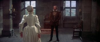 Movie still from “Mary, Queen of Scots” (1971), directed by Charles Jarrott – A man and a woman standing in front of a stone wall; Wide shot, Over the shoulder angle