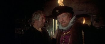 Movie still from “Mary, Queen of Scots” (1971), directed by Charles Jarrott – A man with a beard and a hat is standing next to another man with a beard; Close Up shot, Over the shoulder angle