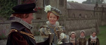 Movie still from “Mary, Queen of Scots” (1971), directed by Charles Jarrott – A woman wearing a hat and holding two silver cups; Medium shot, Low angle