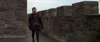 Movie still from “Mary, Queen of Scots” (1971), directed by Charles Jarrott – A man dressed in medieval garb standing in front of a stone wall; Medium shot, Low angle