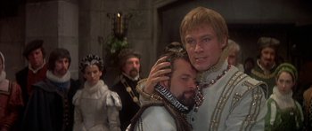 Movie still from “Mary, Queen of Scots” (1971), directed by Charles Jarrott – Two men in medieval garb are embracing each other while others look on; Close Up shot, Over the shoulder angle