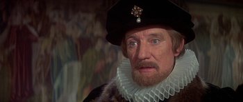Movie still from “Mary, Queen of Scots” (1971), directed by Charles Jarrott – An older man wearing a black hat and a white collar; Close Up shot, Over the shoulder angle