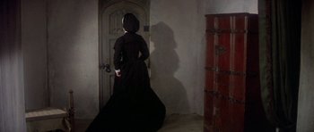 Movie still from “Mary, Queen of Scots” (1971), directed by Charles Jarrott – A woman dressed in black standing in front of a door; Wide shot, High angle