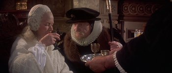 Movie still from “Mary, Queen of Scots” (1971), directed by Charles Jarrott – A man wearing a hat and a fur coat holding a wine goblet; Close Up shot, Over the shoulder angle