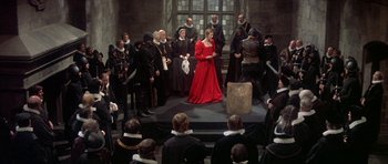 Movie still from “Mary, Queen of Scots” (1971), directed by Charles Jarrott – A woman in a red dress on a stage surrounded by people; Wide shot, High angle