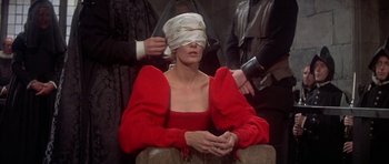 Movie still from “Mary, Queen of Scots” (1971), directed by Charles Jarrott – A blindfolded woman sitting on a chair in front of two other people; Medium shot, Over the shoulder angle