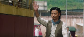 Movie still from “Master Z: The Ip Man Legacy” (2018), directed by Woo-Ping Yuen – A man waving at the camera while standing in front of a train; Medium shot, Low angle