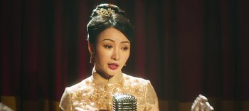 Movie still from “Master Z: The Ip Man Legacy” (2018), directed by Woo-Ping Yuen – A woman in a white dress is holding a microphone; Close Up shot, Over the shoulder angle