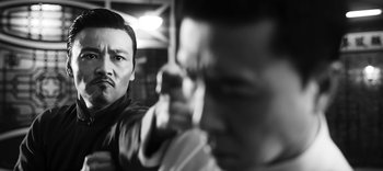 Movie still from “Master Z: The Ip Man Legacy” (2018), directed by Woo-Ping Yuen – A black and white photo of a man holding a gun; Close Up shot, Over the shoulder angle