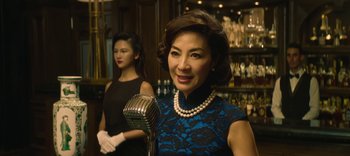 Movie still from “Master Z: The Ip Man Legacy” (2018), directed by Woo-Ping Yuen – A woman in a blue and black dress holding a microphone; Close Up shot, Over the shoulder angle