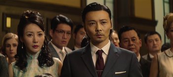Movie still from “Master Z: The Ip Man Legacy” (2018), directed by Woo-Ping Yuen – A man in a suit standing in front of a group of people; Close Up shot, Low angle