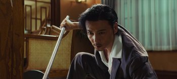 Movie still from “Master Z: The Ip Man Legacy” (2018), directed by Woo-Ping Yuen – A man holding a cane while sitting on the ground; Medium shot, Low angle