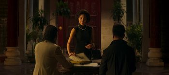 Movie still from “Master Z: The Ip Man Legacy” (2018), directed by Woo-Ping Yuen – A woman standing at a table talking to two people; Medium shot, Over the shoulder angle