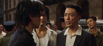 Movie still from “Master Z: The Ip Man Legacy” (2018), directed by Woo-Ping Yuen – A man and two men standing next to each other in front of a group of people; Close Up shot, Over the shoulder angle