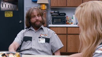 Movie still from “Masterminds” (2015), directed by Jared Hess – A man with a long beard sitting at a table talking to a woman in a kitchen; Medium shot, Over the shoulder angle