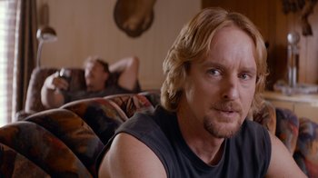 Movie still from “Masterminds” (2015), directed by Jared Hess – A person sitting on a couch near another person; Close Up shot, Over the shoulder angle