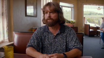Movie still from “Masterminds” (2015), directed by Jared Hess – A man sitting at a table in a room; Medium shot, Over the shoulder angle