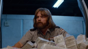 Movie still from “Masterminds” (2015), directed by Jared Hess – A man sitting in front of a pile of money; Medium shot, Low angle