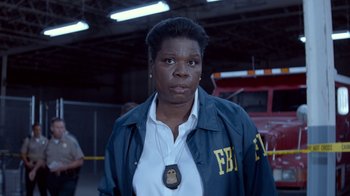 Movie still from “Masterminds” (2015), directed by Jared Hess – A woman wearing a blue jacket with an fbi badge on it; Close Up shot, Over the shoulder angle