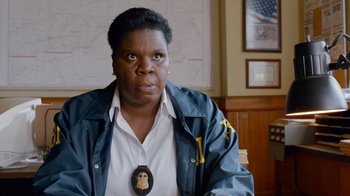 Movie still from “Masterminds” (2015), directed by Jared Hess – A woman with a police badge around her neck sitting in front of a map; Close Up shot, Over the shoulder angle