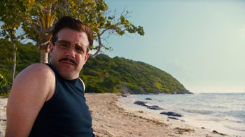 Movie still from “Masterminds” (2015), directed by Jared Hess – A man with a beard and glasses on a beach; Close Up shot, Low angle