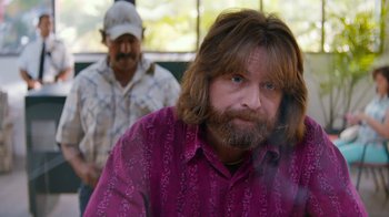 Movie still from “Masterminds” (2015), directed by Jared Hess – A man with long hair and a beard wearing a purple shirt; Close Up shot, Over the shoulder angle