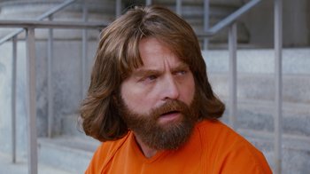 Movie still from “Masterminds” (2015), directed by Jared Hess – A man with long hair and beard wearing an orange t - shirt; Close Up shot, Over the shoulder angle