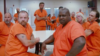 Movie still from “Masterminds” (2015), directed by Jared Hess – A group of men in orange jumpsuits sitting at a table; Medium shot, High angle