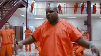 Movie still from “Masterminds” (2015), directed by Jared Hess – A man in an orange prison uniform stands in an orange jail cell; Medium shot, Low angle