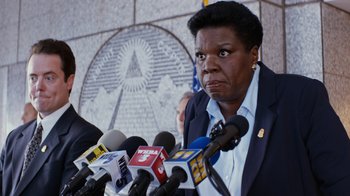 Movie still from “Masterminds” (2015), directed by Jared Hess – A woman standing in front of microphones in front of a wall; Close Up shot, Low angle