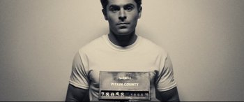Movie still from “Extremely Wicked, Shockingly Evil and Vile” (2019), directed by Joe Berlinger – Black and white photograph of a man in a police mugshot; Medium shot, Low angle