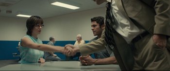 Movie still from “Extremely Wicked, Shockingly Evil and Vile” (2019), directed by Joe Berlinger – Two men shaking hands in a room with people sitting around it; Medium shot, Over the shoulder angle