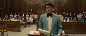 Movie still from “Extremely Wicked, Shockingly Evil and Vile” (2019), directed by Joe Berlinger – A man wearing a suit and tie in front of a crowd of onlookers in a court room; Medium shot, Over the shoulder angle
