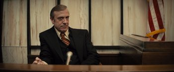 Movie still from “Extremely Wicked, Shockingly Evil and Vile” (2019), directed by Joe Berlinger – An older man wearing a suit and tie sitting in front of a microphone; Medium shot, Over the shoulder angle