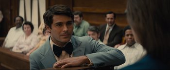 Movie still from “Extremely Wicked, Shockingly Evil and Vile” (2019), directed by Joe Berlinger – A man in a suit and bow tie in front of other men; Medium shot, Over the shoulder angle