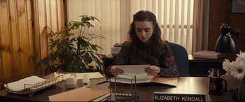 Movie still from “Extremely Wicked, Shockingly Evil and Vile” (2019), directed by Joe Berlinger – A woman sitting at a desk looking down at a piece of paper; Medium shot, Over the shoulder angle