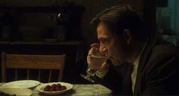 Movie still from “Matewan” (1987), directed by John Sayles – A man sitting at a table drinking a glass of water; Medium shot, Over the shoulder angle