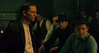 Movie still from “Matewan” (1987), directed by John Sayles – A group of men sitting in a dark room; Medium shot, Over the shoulder angle