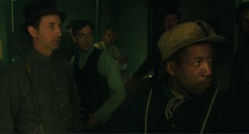 Movie still from “Matewan” (1987), directed by John Sayles – A group of men standing next to each other in a dark room; Medium shot, Over the shoulder angle