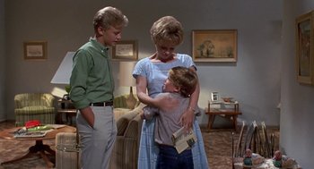 Movie still from “Matinee” (1993), directed by Joe Dante – A man and a woman hug a boy in a living room; Medium shot, Over the shoulder angle
